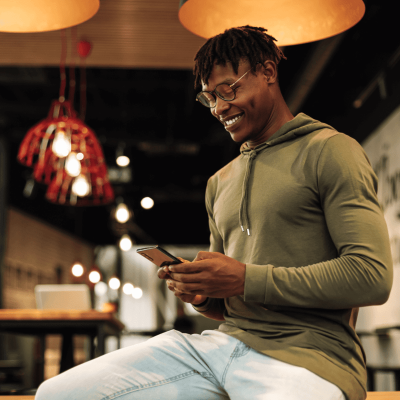 Man wearing glasses and a green hoodie in a cafe using mobile phone to access the commodity profit calculator